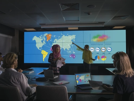 People in a conference room listening to a presentation with geographical data projected on a screen.
