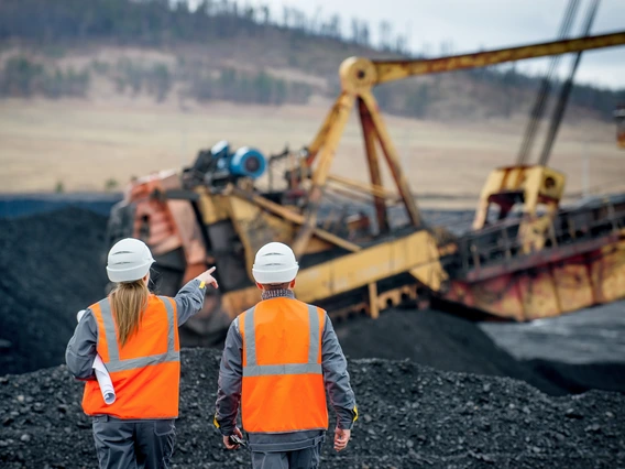 Two mining workers looking at large mining equipment in use