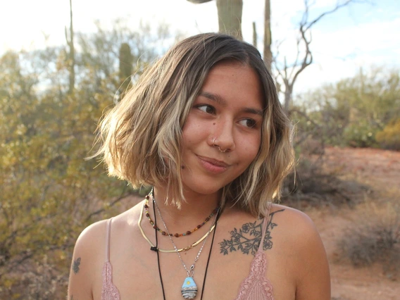 An up-close picture of Maya gazing to the side of the camera. She is standing on a desert trail in Ariozna which cacti in the background.