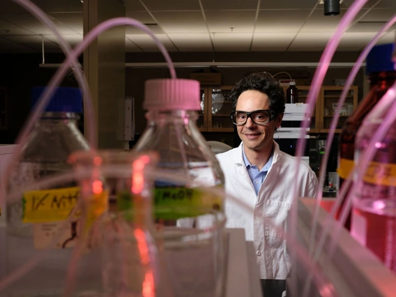 Andrea Achilli stands in lab with lab coat and equiptment.