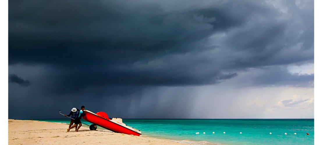 storm approaching beach where two men stand with boat