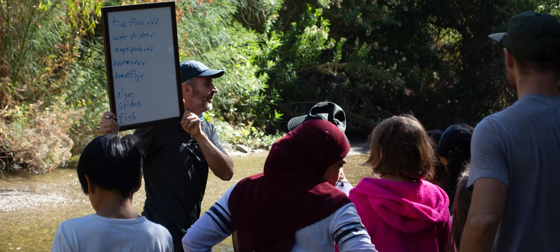 Michael Bogan holding a sign in front of students on field trip to the Santa Cruz river.