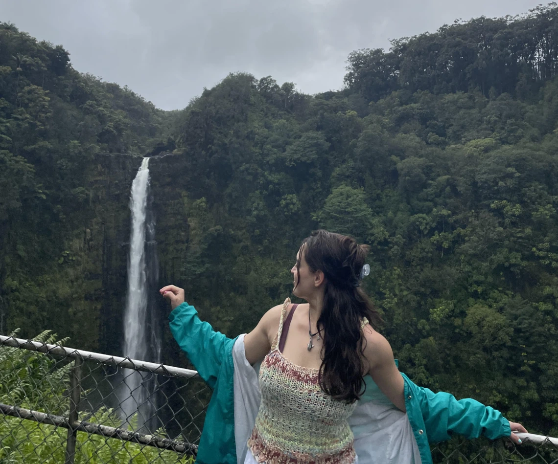 Isabella looking at the tropical land behind her. There is a large waterfall in the distance.