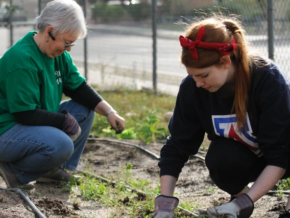 Two women pulling weeds in a garden together on a cool fall day