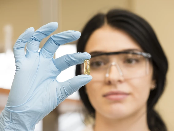 A scientist closely inspecting a pill with gloves and safety goggles on