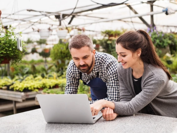 Two researchers in a massive greenhouse looking at a laptop 