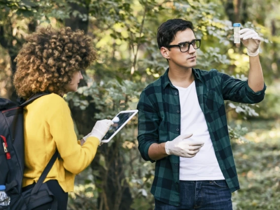 Two students in a forest examining a sample