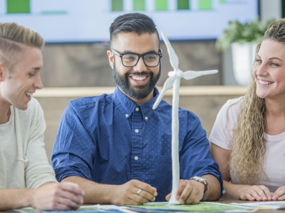 Three students happily examining a wind turbine model