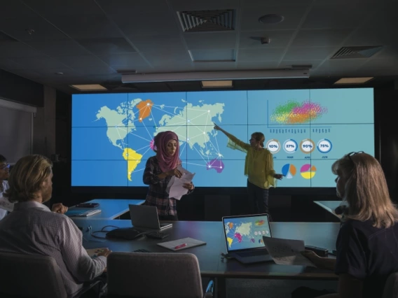 People in a conference room listening to a presentation with geographical data projected on a screen.