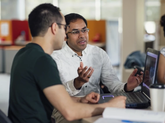 Two people discussing a project while looking at a laptop screen