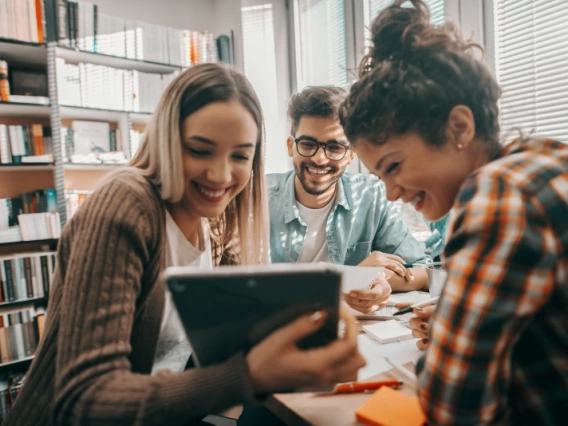 Three students looking happily at data on a tablet