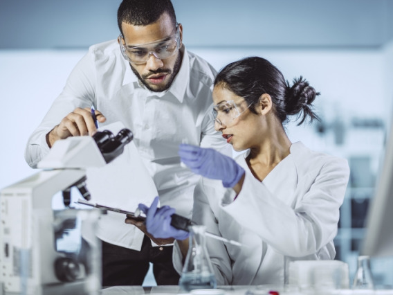 Two scientists examining and taking notes on samples being analyzed under a microscope