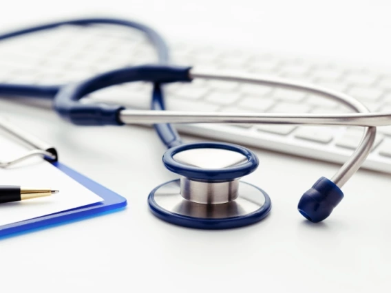 A stethoscope, keyboard, and a clipboard with a pen resting on top