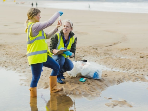 Two researchers gathering a water sample from a beach