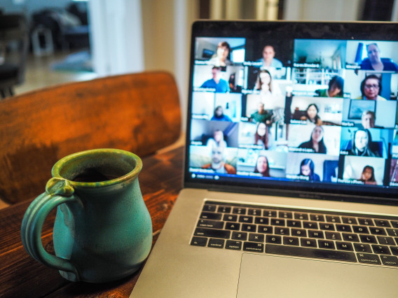 A coffee cup next to a laptop with a Zoom webinar on the screen