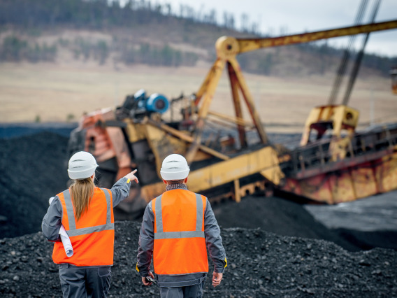 Two mining workers looking at large mining equipment in use