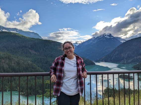 Lexis smiling as she is at a look out point. The view behind her is of green mountains with snow at the tops and a large greenish blue lake.