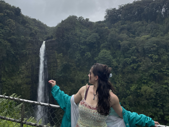 Isabella looking at the tropical land behind her. There is a large waterfall in the distance. 
