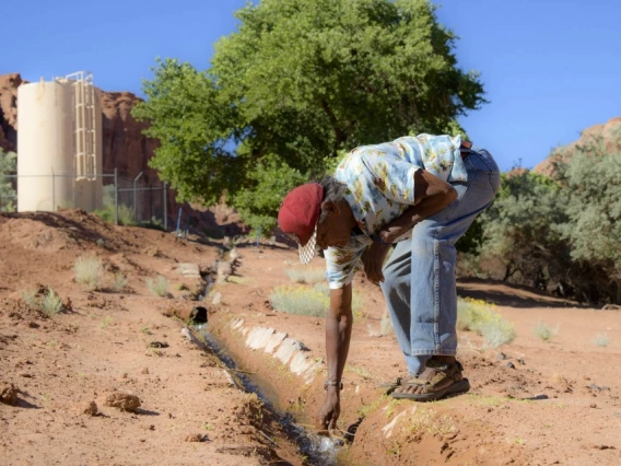 A man leaning over a small stream of water on the Navajo Nation