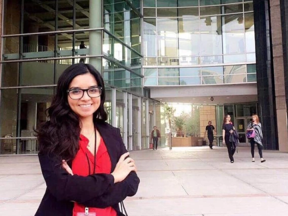 Woman smiling in red shirt standing in front of glass building.