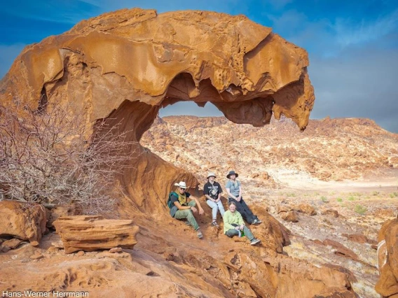 Four students sit under a natural overhang in the desert