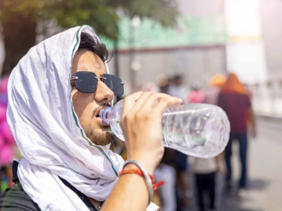 Man with head covered drinks from water bottle