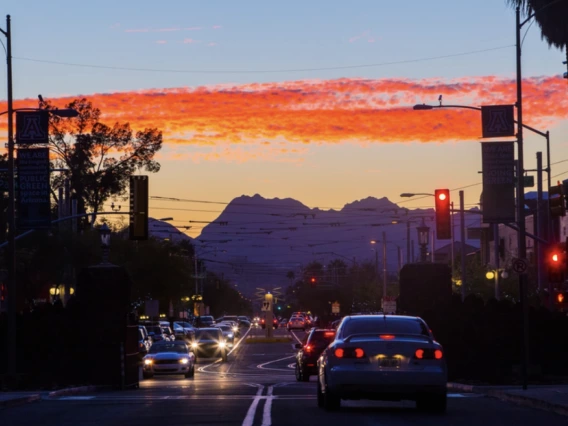 Cars drive at sunset with mountains in the background.