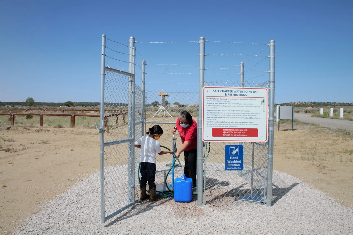 An image of a mother and daughter filling a container with water from a safe water point in the Navajo Nation