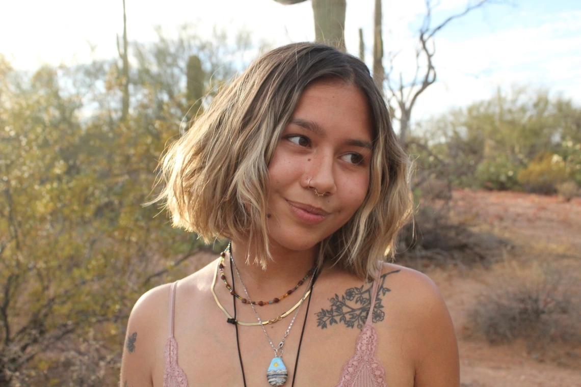 An up-close picture of Maya gazing to the side of the camera. She is standing on a desert trail in Ariozna which cacti in the background.