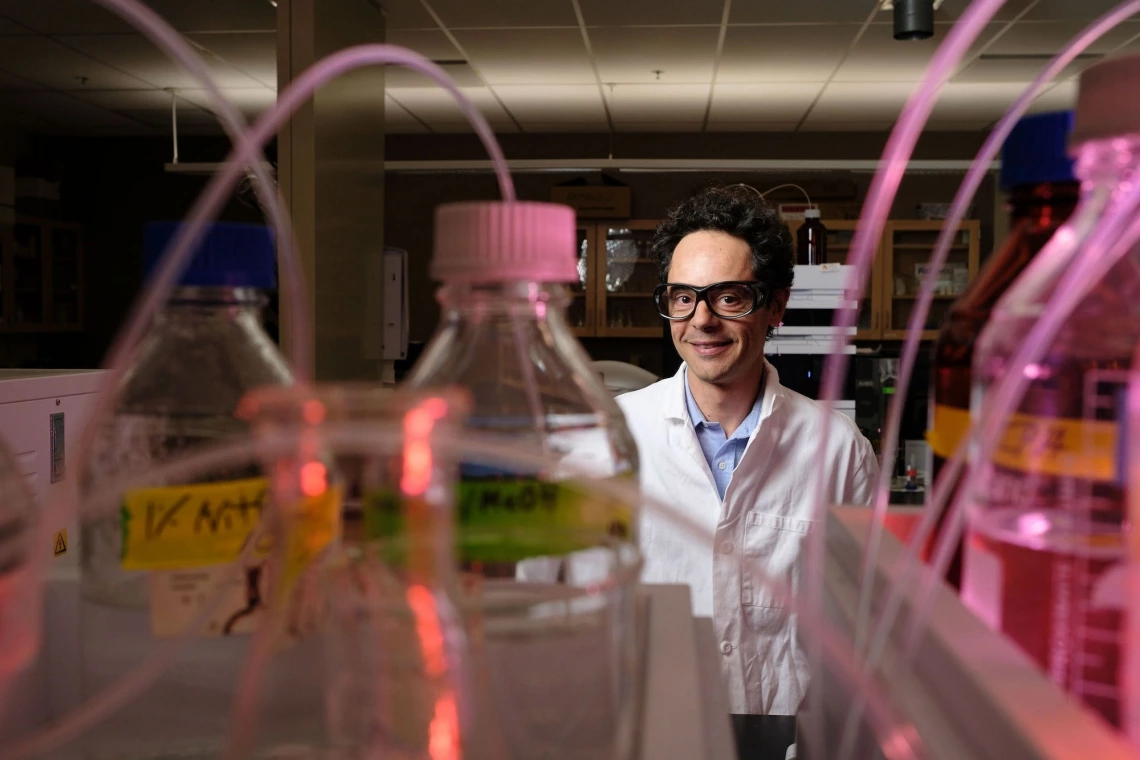 Andrea Achilli stands in lab with lab coat and equiptment.