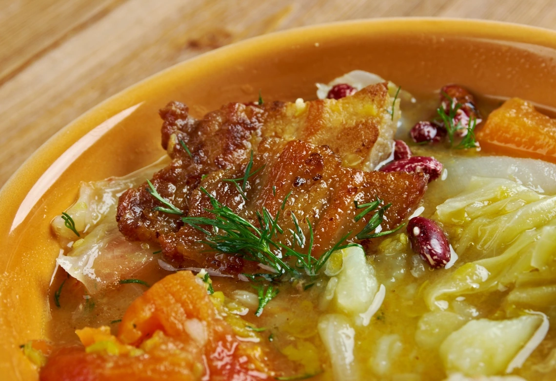 A close up of a stew containing meat, vegetables and beans