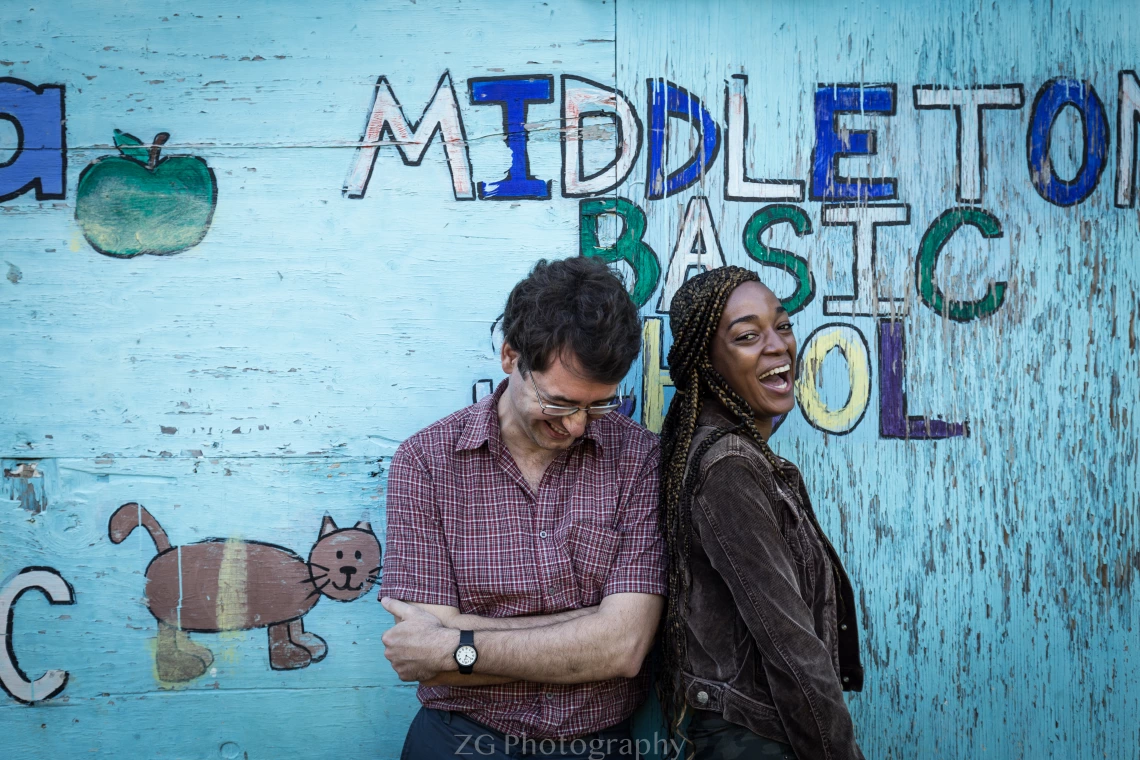 Man and woman stand laughing in front of blue school building