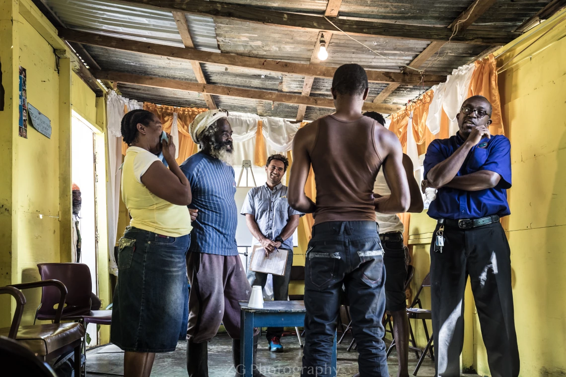 Group of Jamaican men and women stand in a circle inside a yellow room.