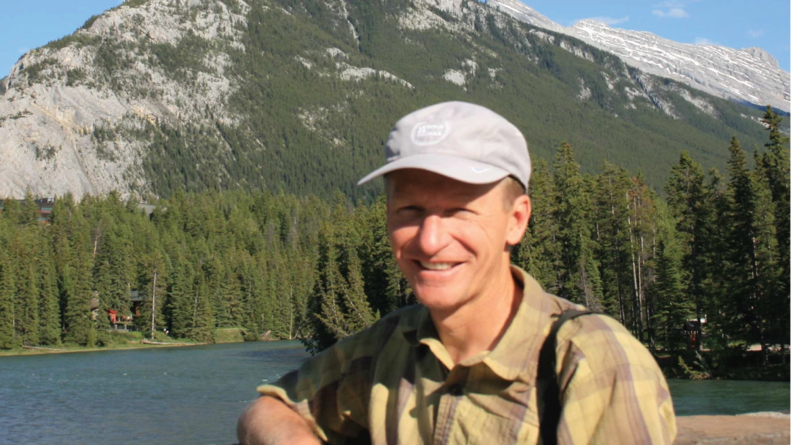 Abe Springer in hat in front of mountain lake.