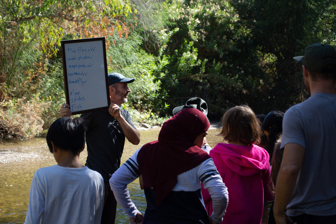 Michael Bogan holding a sign in front of students on field trip to the Santa Cruz river.