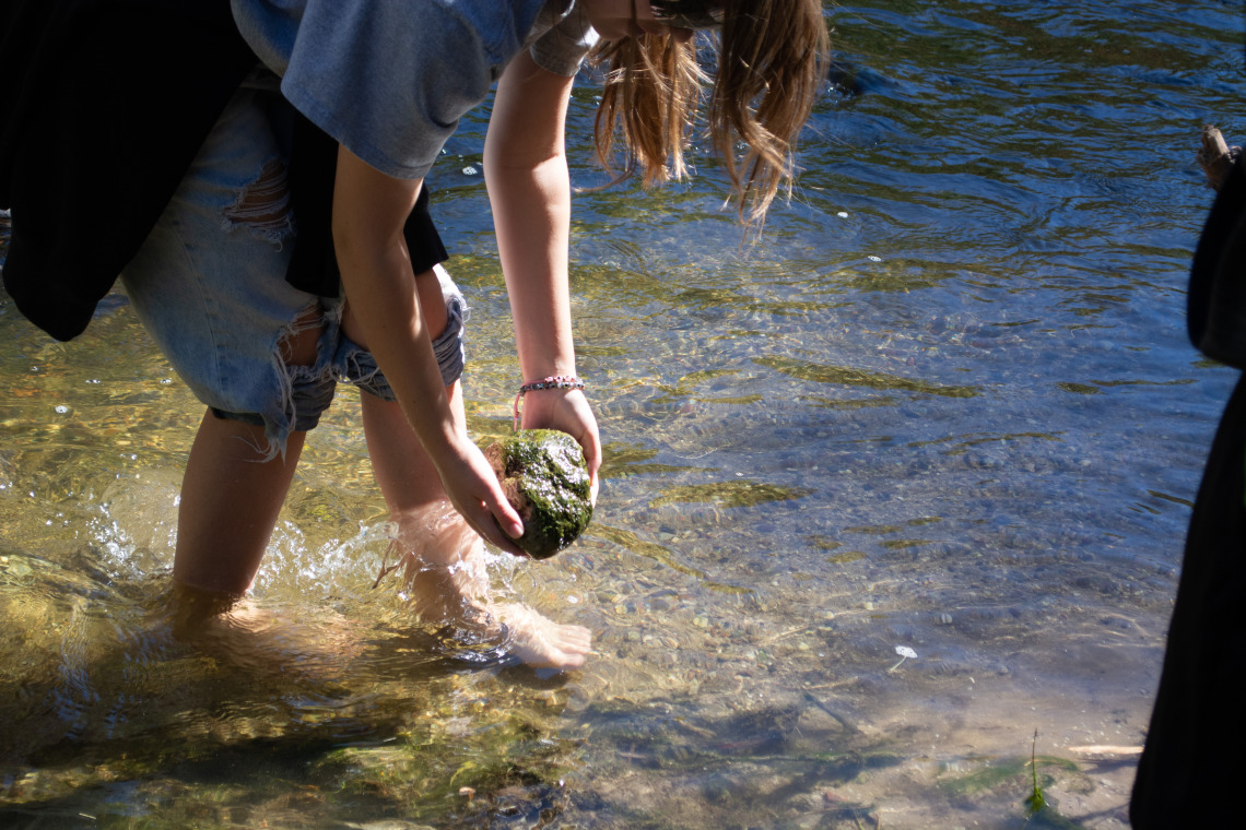 A barefoot student examines a rock in the Santa Cruz River.