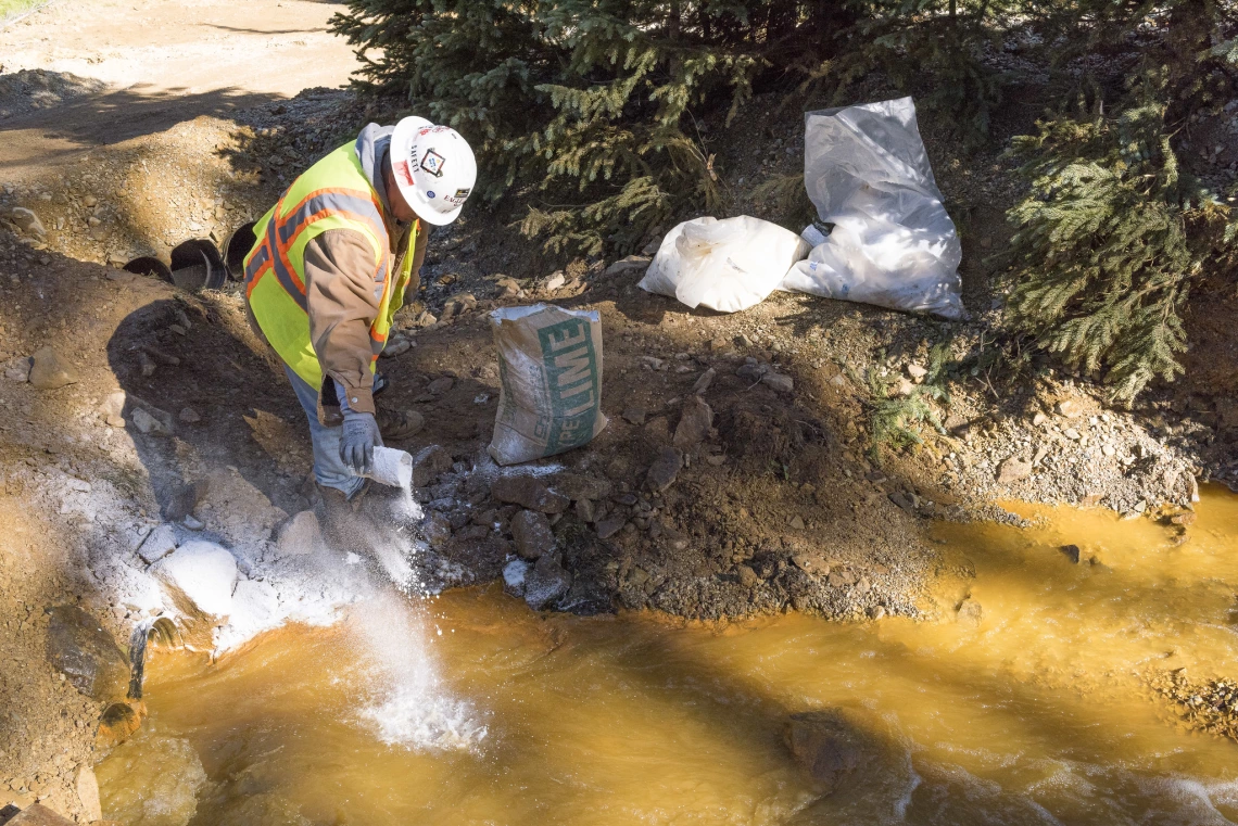 A worker adds lime to a settling pond.