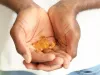 Close-up of a person holding several yellow softgel capsules in cupped hands, with a light green background. The image suggests a focus on health, wellness, or supplements.